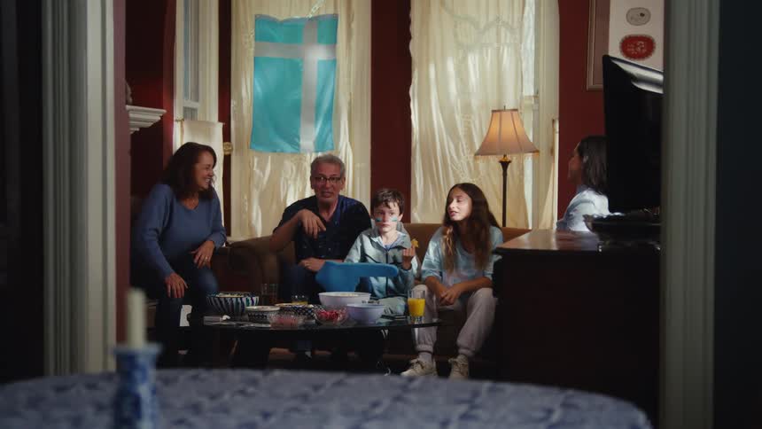 A happy multi-generational family cheers and celebrates together while watching a sports game on TV in their living room