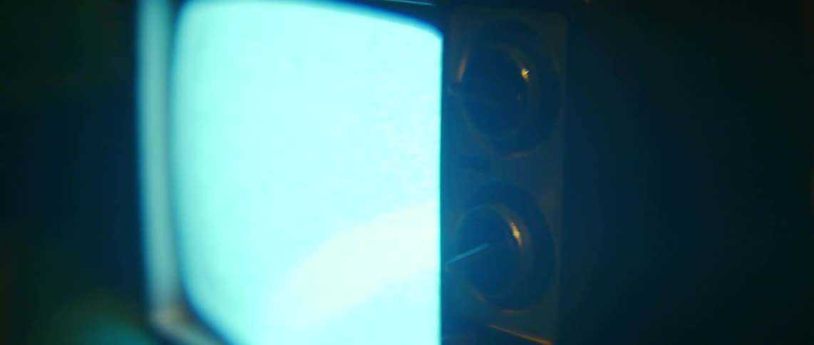 An old television set with a glowing blue static screen sits in a dark, atmospheric room