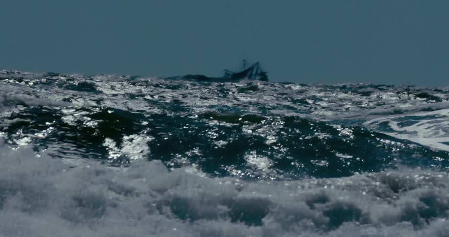 Dramatic slow motion footage of a powerful, turbulent sea with a lone fishing boat on the stormy horizon
