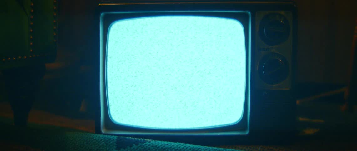 The glowing blue screen of a retro portable television shows static noise in a dimly lit environment