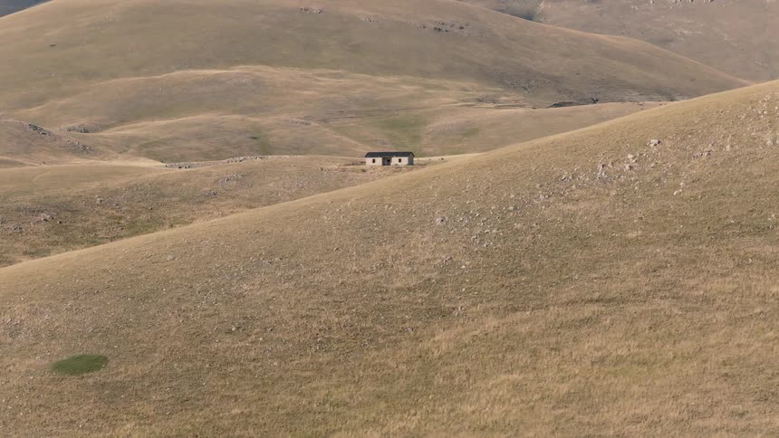 A slow aerial push-in reveals an isolated and abandoned stone house in a vast, arid, and hilly landscape
