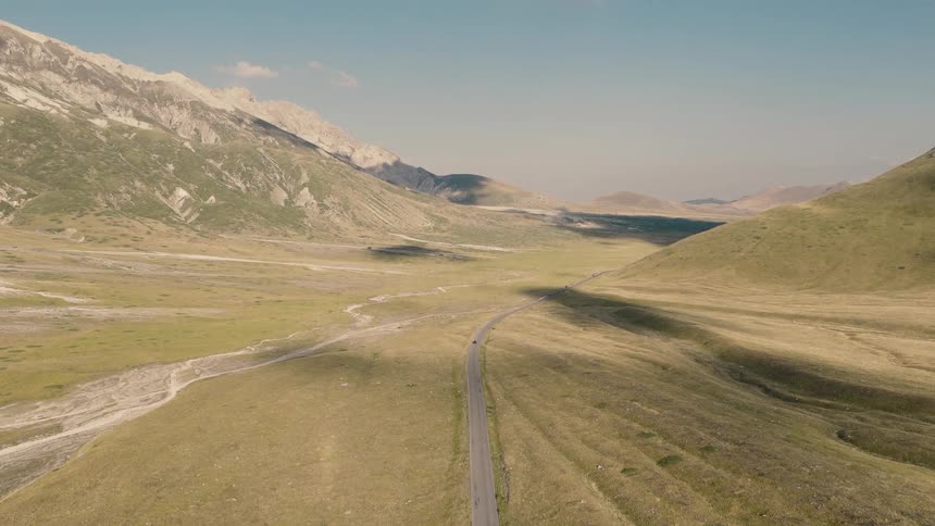 An expansive aerial view reveals a solitary road winding through a vast valley nestled between majestic mountain ranges