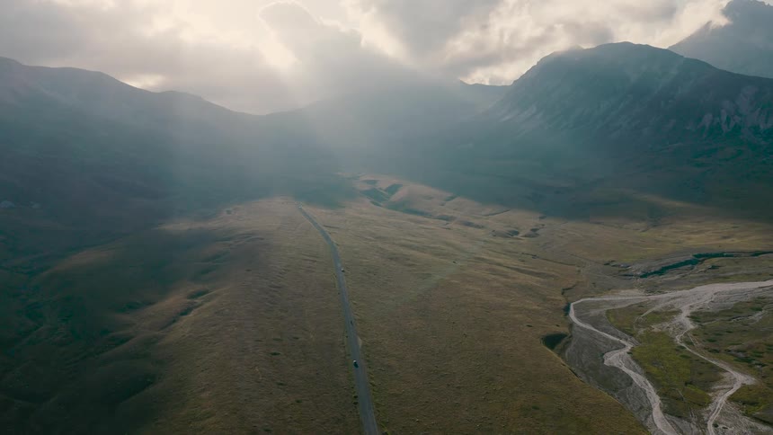 An epic aerial view of a remote road through a misty mountain valley illuminated by beautiful sun rays