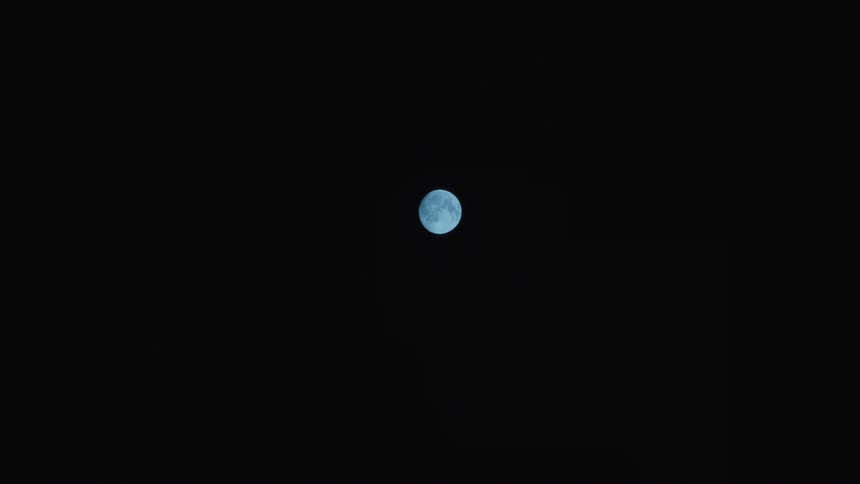 A static shot shows a full blue moon shining brightly in the center of a pitch-black night sky
