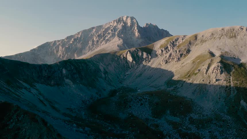 An epic aerial view flies through thick clouds to reveal a stunning mountain range at sunrise