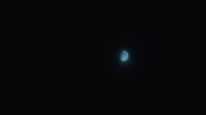 A static shot of a glowing blue half-moon in the vast darkness of the night sky