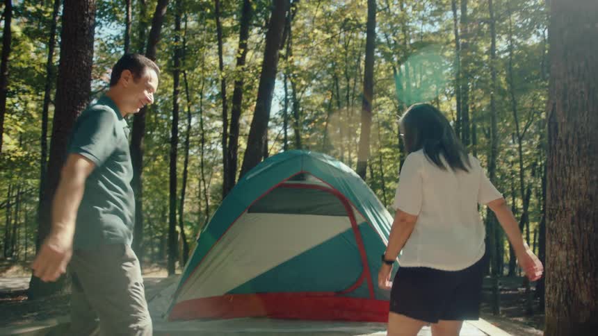 A happy couple gives a slow-motion high-five after successfully setting up their tent at a sunny forest campsite