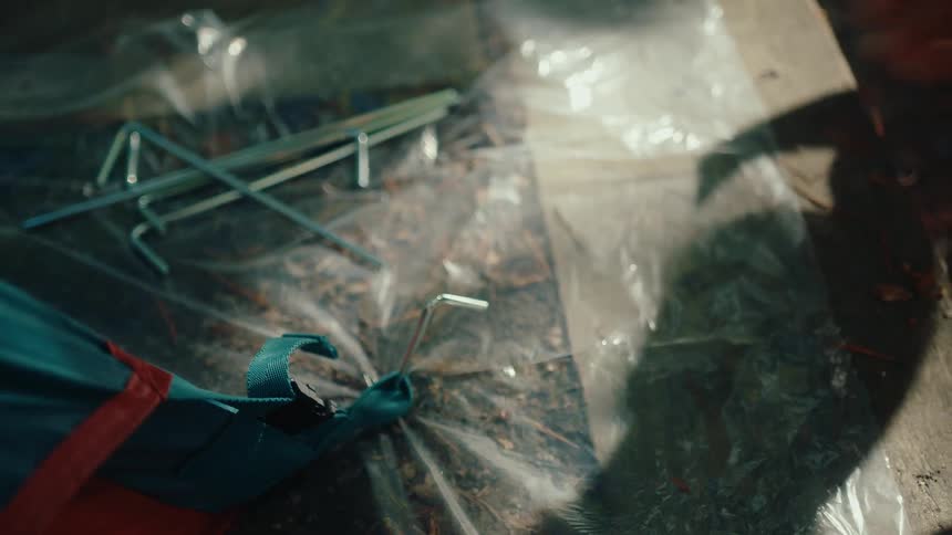 Close-up of a camper's hands using a hammer to drive a metal stake into the ground, securing a tent at the campsite