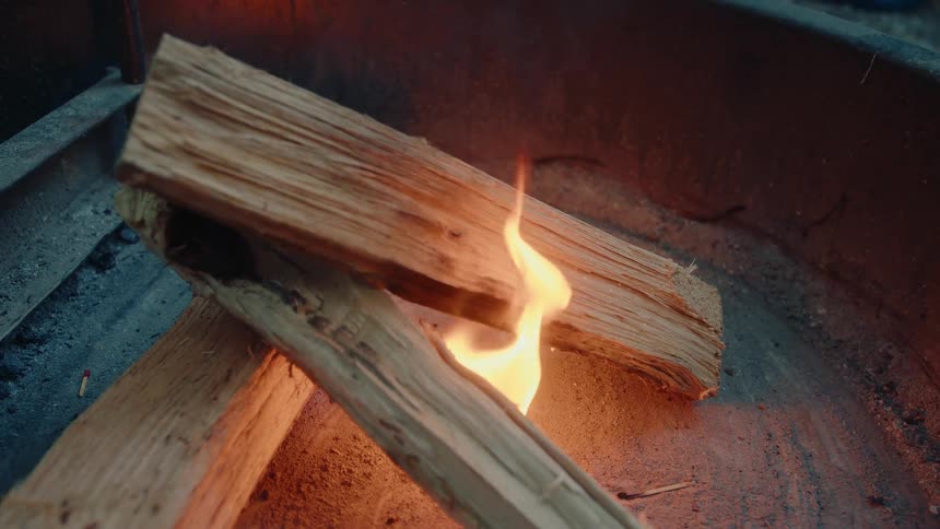 Close-up of a small flame slowly growing on chopped firewood in a metal campfire pit