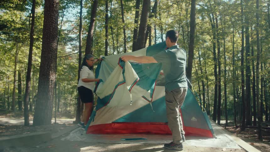 A mature couple works together setting up a tent at a campsite on a sunny day in the forest