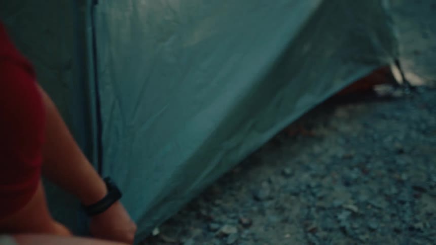 Close-up slow-motion shot of a man setting up his tent at a forested campsite during the day