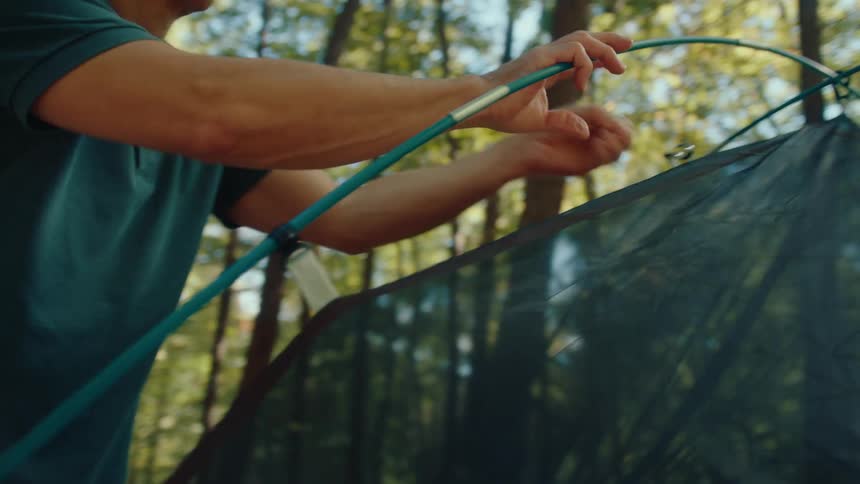 An older couple works together to assemble their tent while camping in a sunlit forest