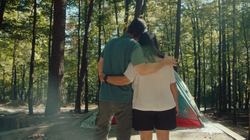 A mature couple lovingly embraces while admiring their sunny campsite in the forest