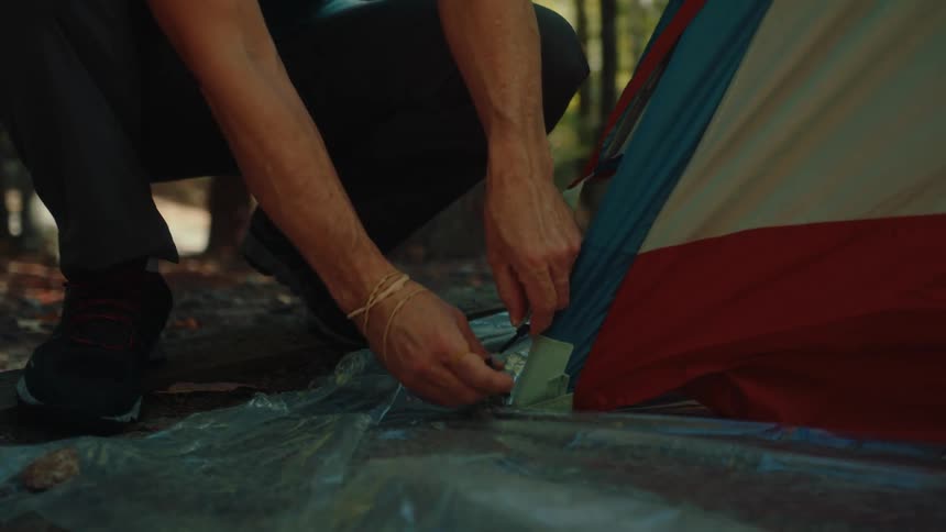 Close up shot of a man setting up a tent in a sunny forest, connecting the poles and securing them to the base