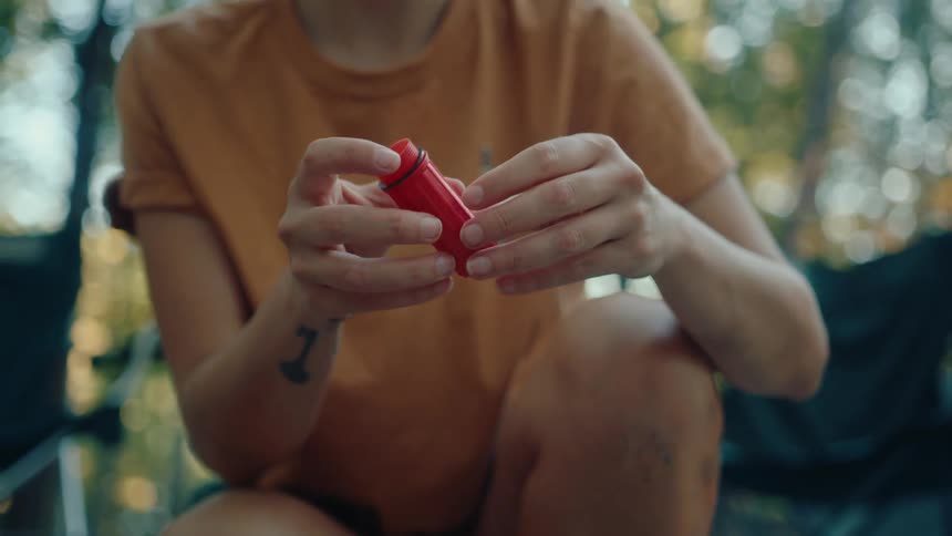 Close-up of a woman opening a waterproof container with matches while camping in the forest