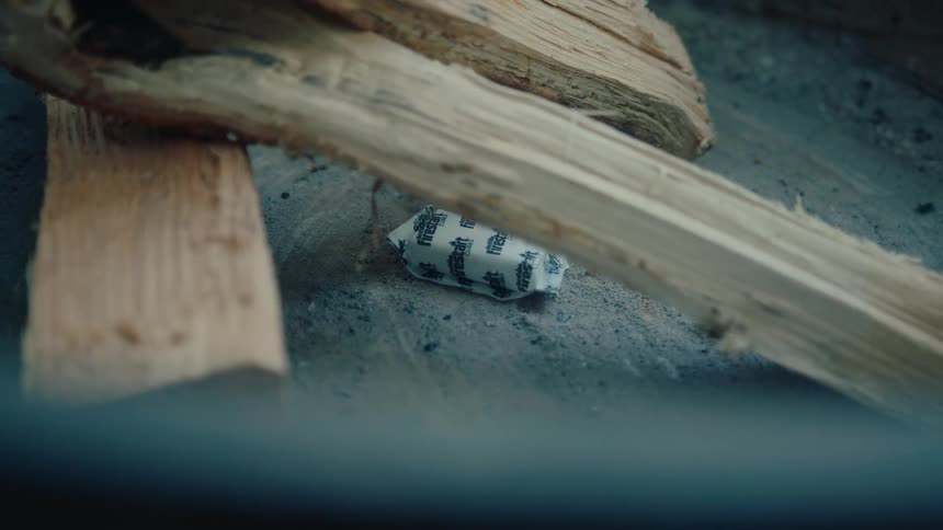 A person places a fire starter packet under logs of wood in a fire pit to start a campfire