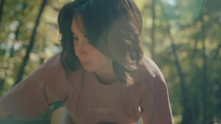 Focused young woman in a pink shirt sets up a camping tent in a sunny green forest