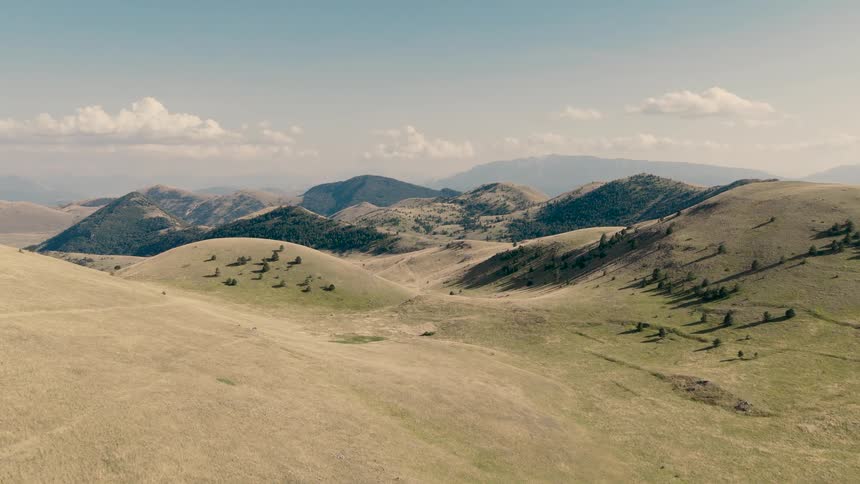 A breathtaking aerial journey flying over vast rolling hills and a beautiful mountain landscape on a clear sunny day