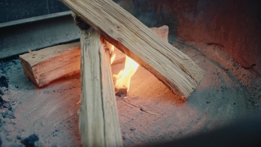 A close-up view of firewood logs slowly catching fire inside a metal fire pit