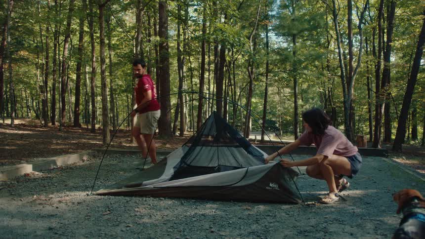 A man and woman assemble their tent together at a beautiful campsite in the woods
