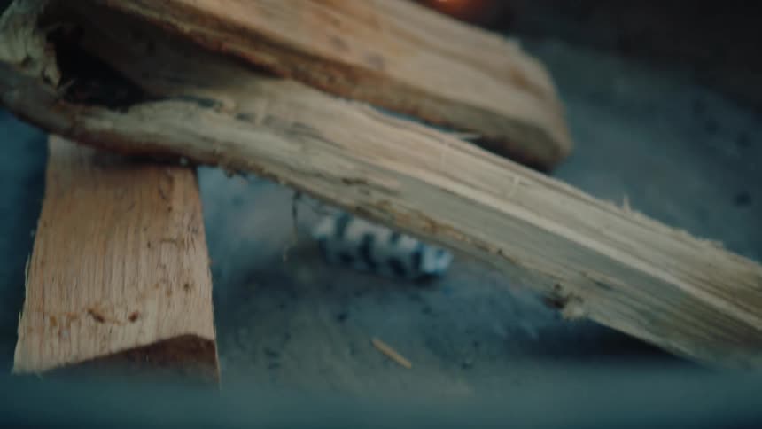 Slow motion close-up of a person striking a match and carefully lighting a fire starter for a campfire