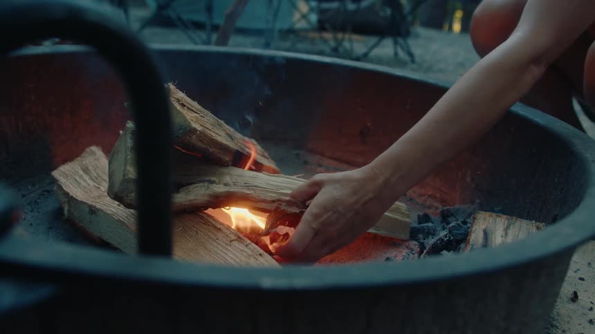 A woman carefully gathers dry leaves to use as kindling, starting a warm and inviting campfire at her wooded campsite