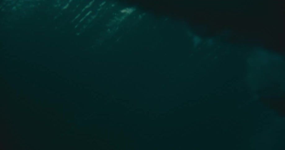 A massive ocean wave crests and breaks over the camera in dramatic slow motion, revealing the dark, turbulent world beneath the surface