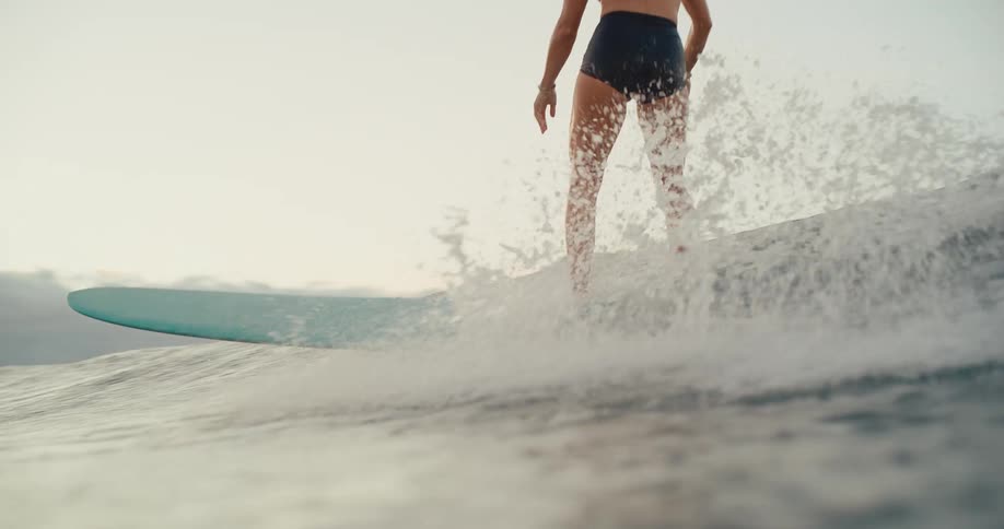 A woman gracefully rides a wave on her surfboard in slow motion, shot from a low water angle that transitions to an underwater view