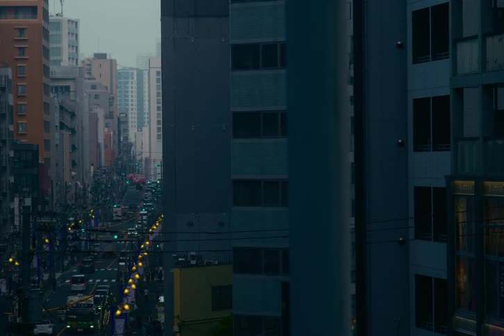 A long view down a busy city street in an Asian metropolis during a moody, overcast evening