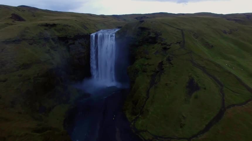 A waterfall flows over green cliffs to a pool below