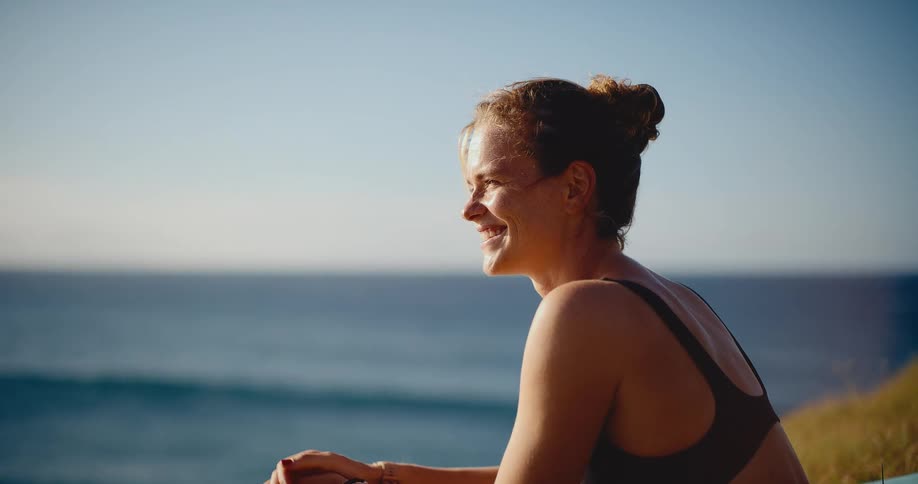 Cinematic slow motion of a beautiful young woman smiling and enjoying the moment on a cliff overlooking the ocean at sunset