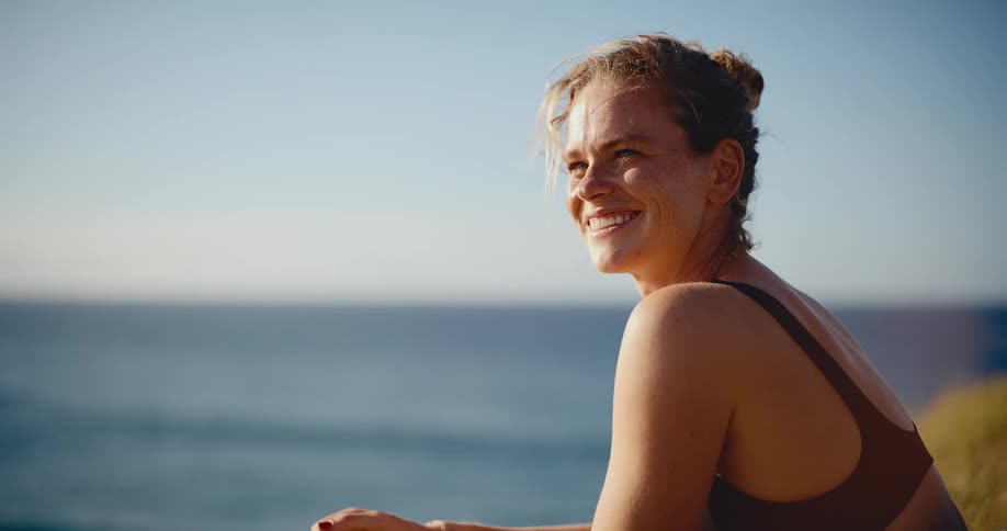 A beautiful young woman with sunscreen on her face smiles and enjoys the view of the ocean at sunset