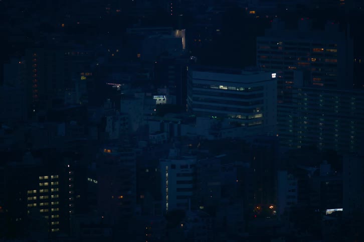 A high-angle timelapse of a dense urban cityscape at night as lights flicker on and off in apartment buildings and offices