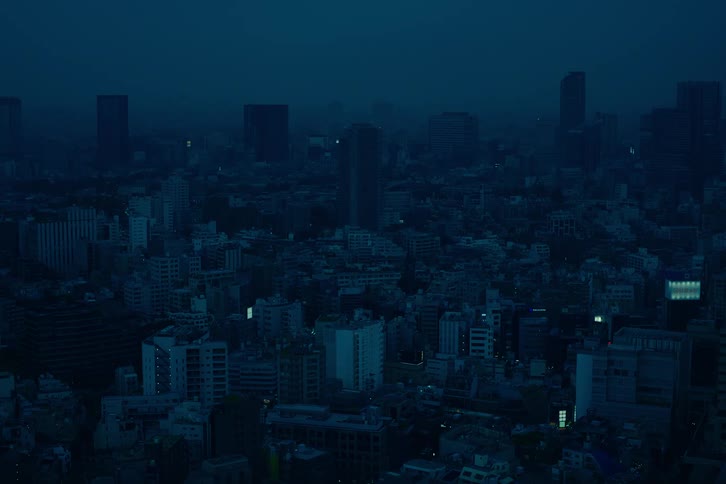 A moody, dark blue high-angle view of a sprawling metropolis at night as a train passes through