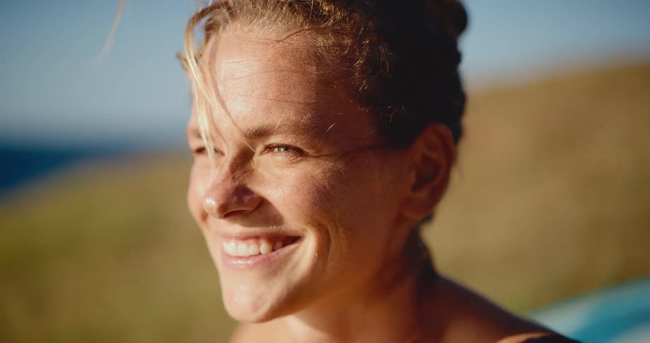 Close-up slow motion portrait of a happy young woman smiling warmly at golden hour with her hair blowing in the wind