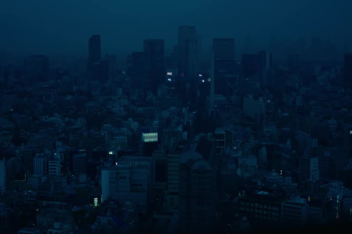 An atmospheric wide shot of a sprawling urban cityscape enveloped in a moody, dark blue haze at night