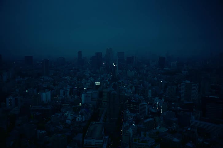A static wide shot of a sprawling, hazy city skyline at night, cast in a deep blue light