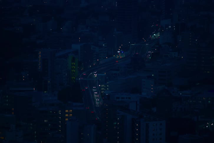 An elevated view shows traffic flowing along a curved highway through a dark cityscape at night