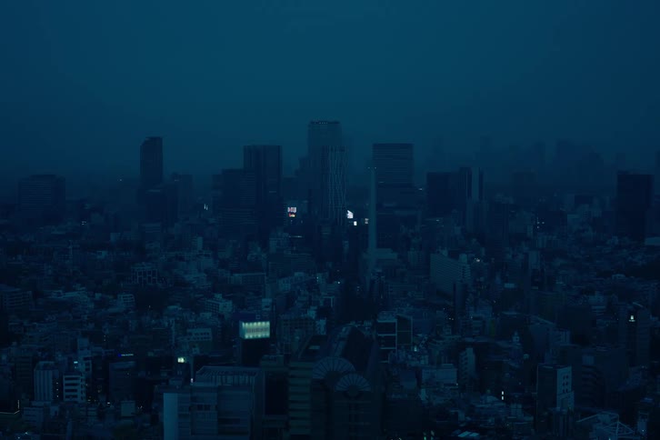 A moody, blue-tinted wide shot of a sprawling city skyline at night, shrouded in a thick fog