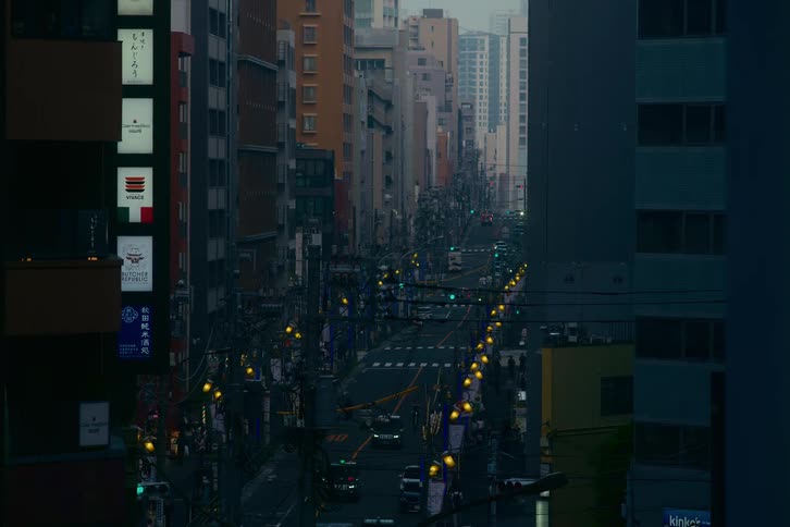 A high-angle view of a dense urban street in Japan at dusk, with traffic moving slowly below