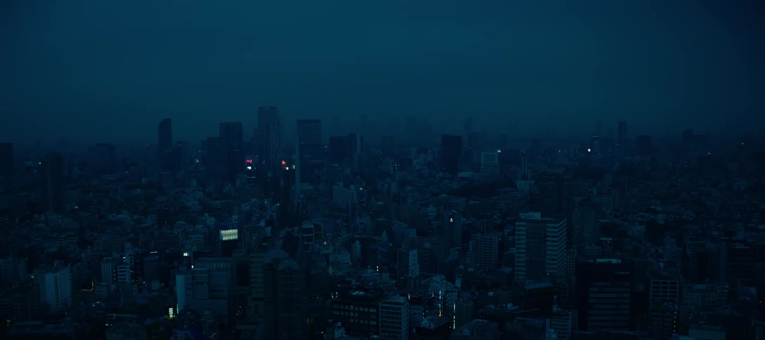 Lightning flashes dramatically in the dark blue sky over a sprawling cityscape during a thunderstorm at night