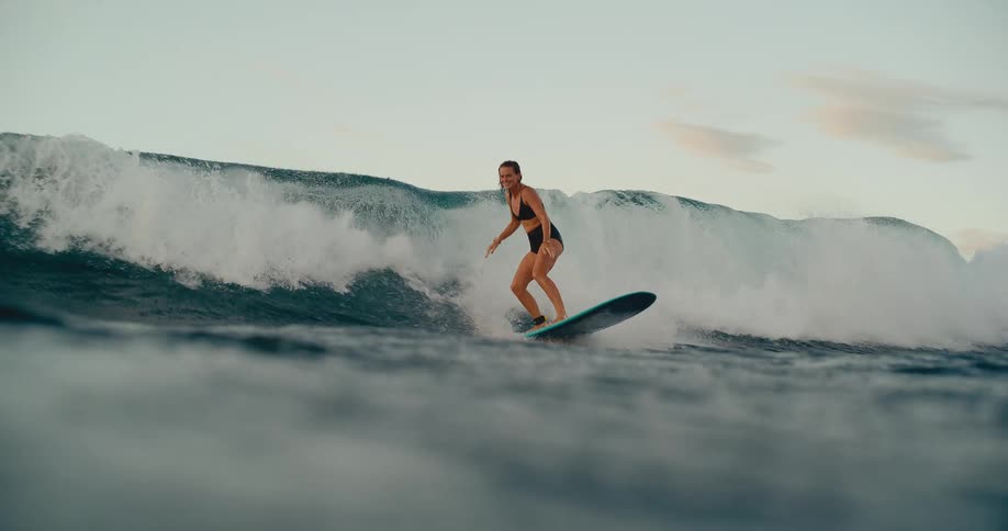 An athletic woman with a joyful expression gracefully surfs a large ocean wave in stunning slow motion
