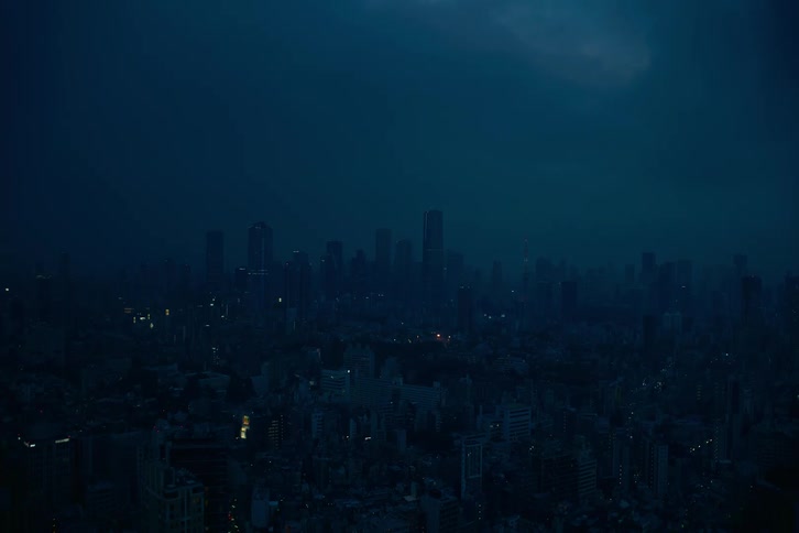 Wide aerial view of a sprawling city skyline shrouded in darkness and haze on a moody night