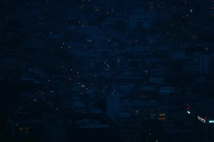 A high-angle static shot captures the quiet atmosphere of a city after dark, with scattered lights twinkling in the distance