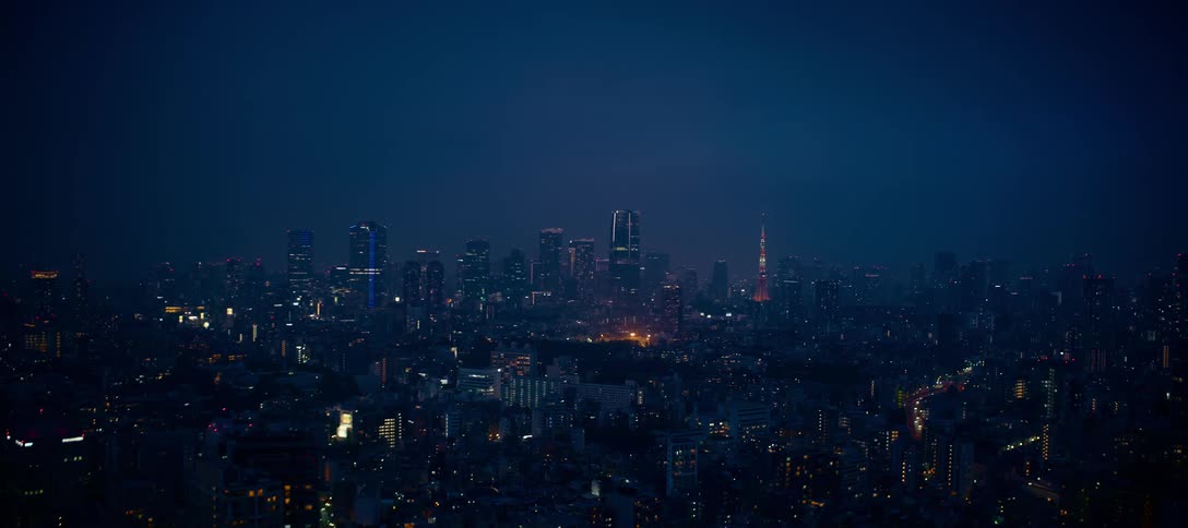 A wide, static shot of the Tokyo cityscape at night with twinkling lights and the iconic Tokyo Tower on the horizon
