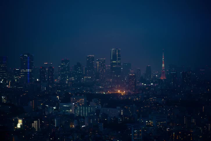 A wide panoramic view of the glowing Tokyo city skyline at night, showcasing the illuminated skyscrapers and the iconic Tokyo Tower