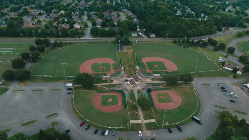 A static high-angle aerial shot captures a community sports park with four baseball diamonds