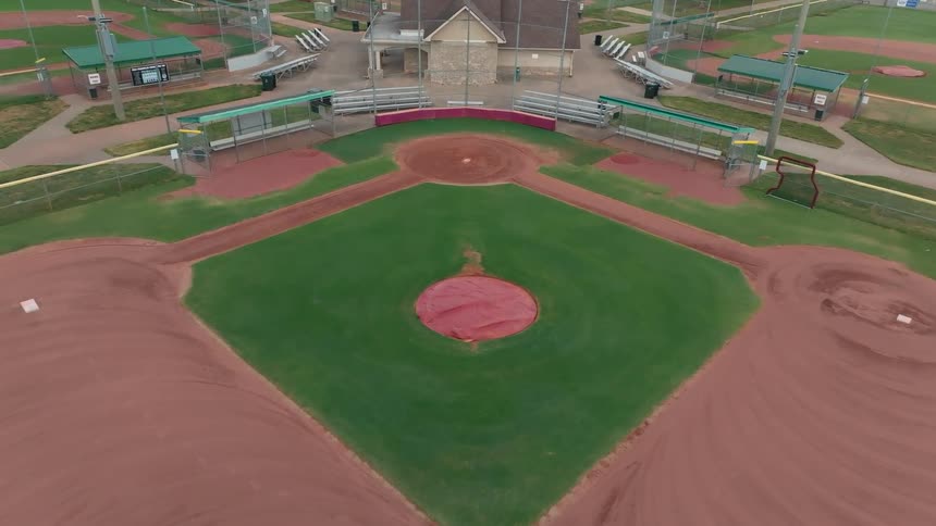 A slow aerial descent over a complex of empty baseball fields, focusing on one pristine diamond ready for a game