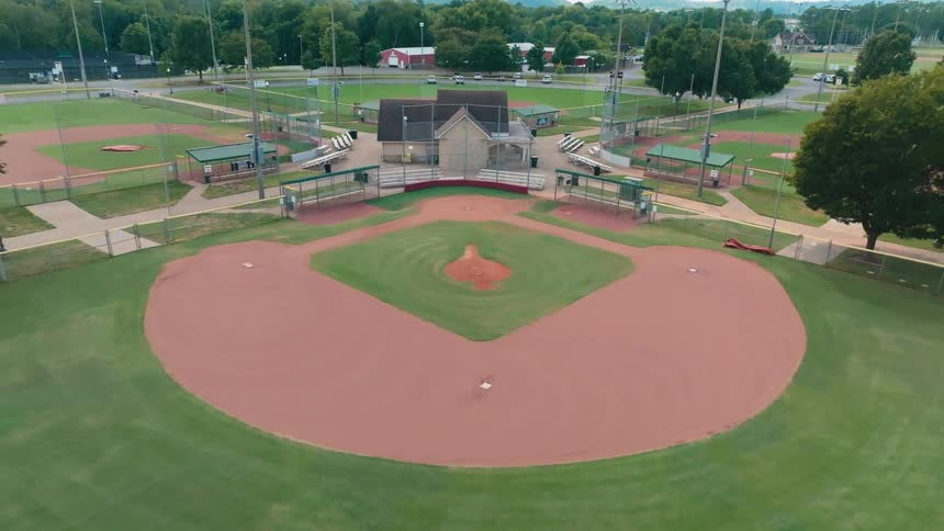 A slow aerial pullback reveals an empty, multi-field baseball and softball complex ready for a game