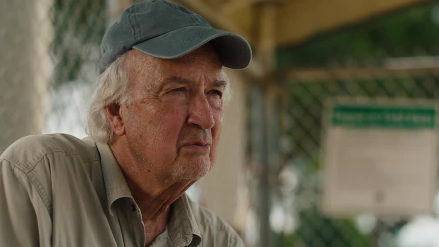 A contemplative elderly man in a baseball cap sits alone, lost in thought